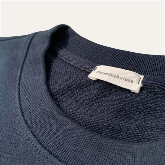close up flat lay Navy blue sweater with a visible twill label on a light gray background