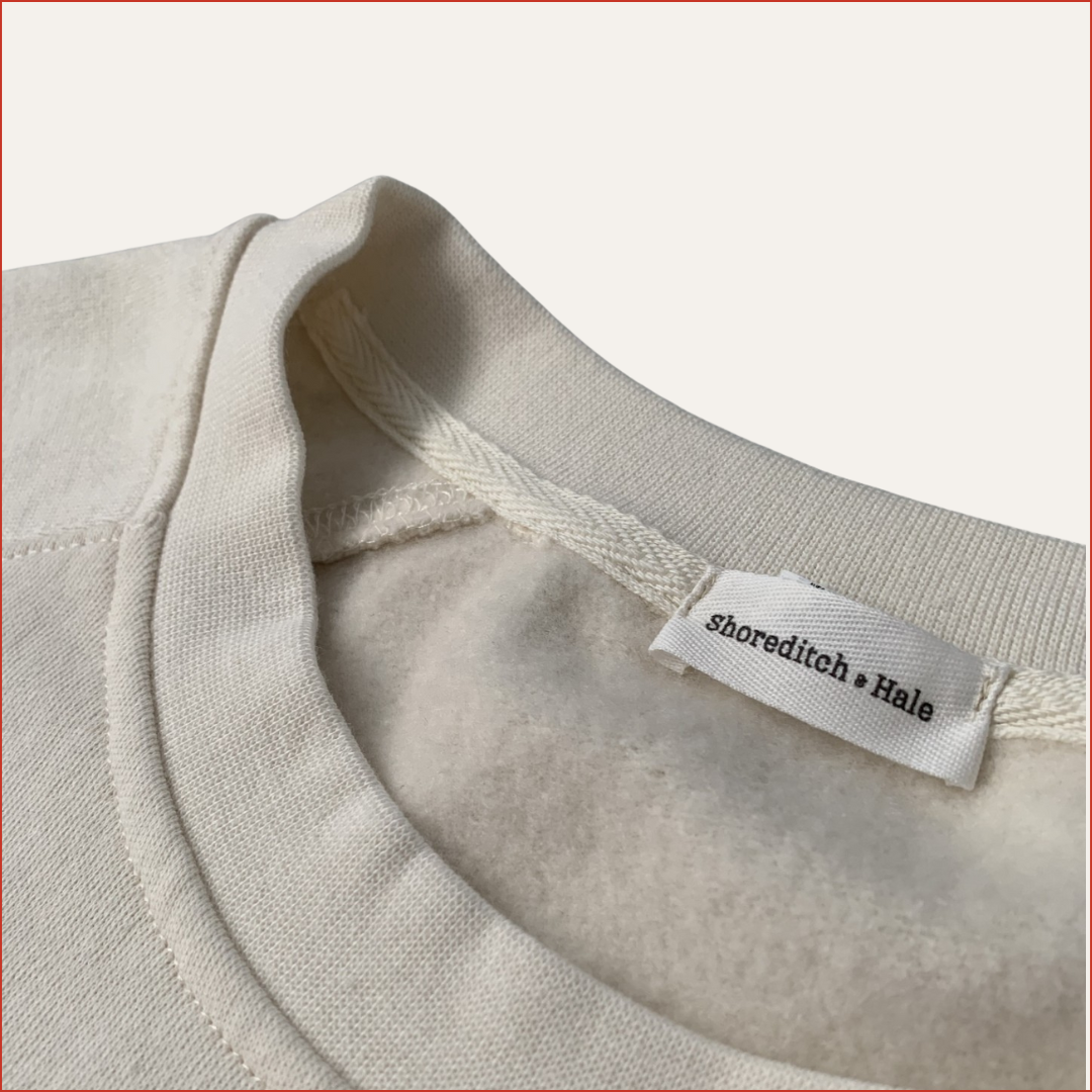 Soft white men's sweatshirt with twill label and minimalist understated design from Shoreditch & Hale – casual modern fit, laid flat.