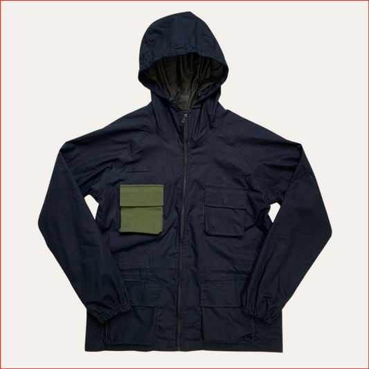 Flat lay phot of a Navy blue jacket with a green pocket on a light gray background by shoreditch and hale minimalist design