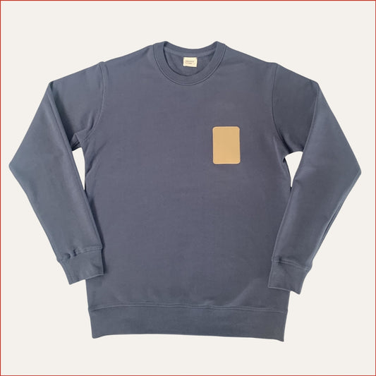 Flat lay image of a Carbon Blue men's sweatshirt with a brown rectangular patch on a light gray background. Minimalist design casual wear by shoreditch and hale