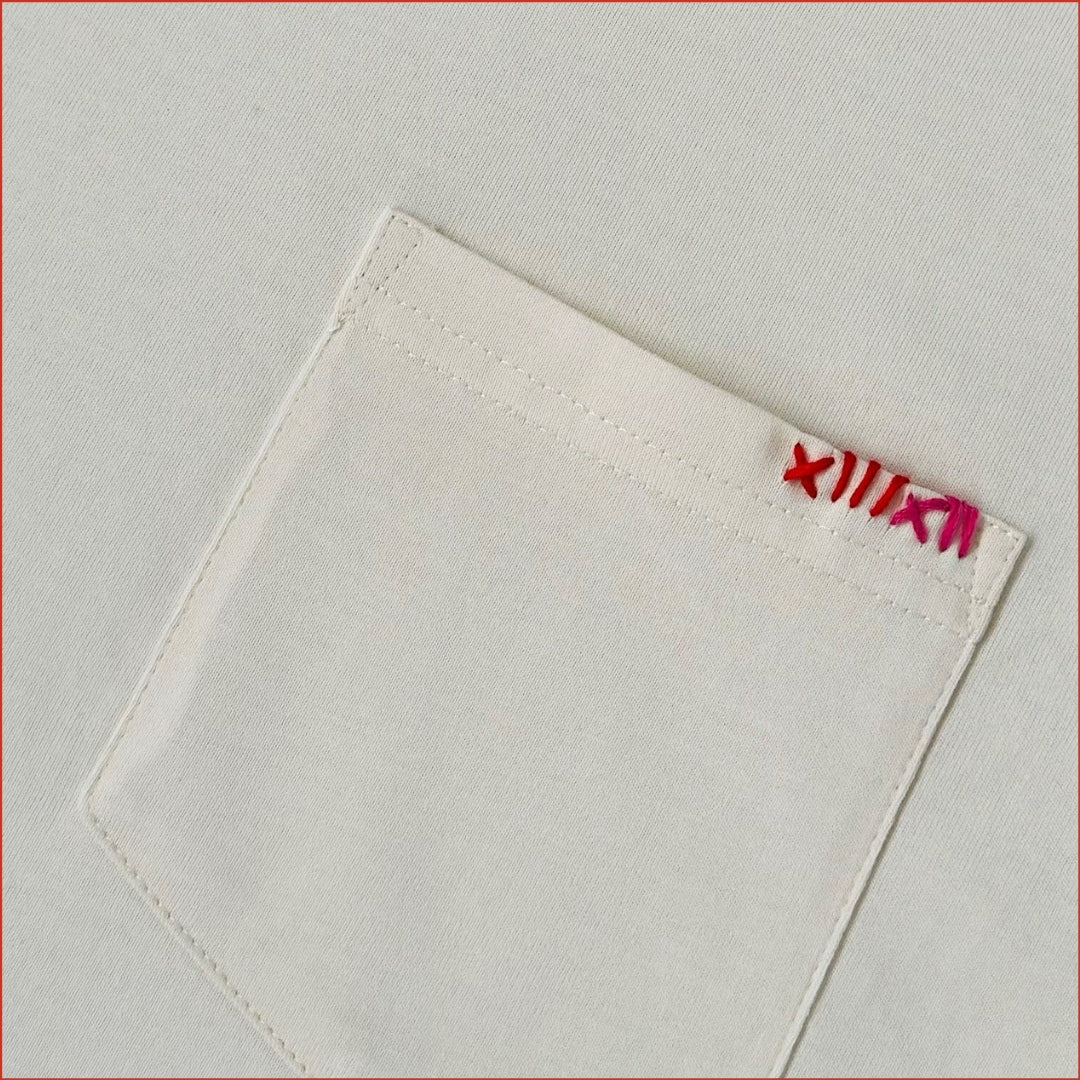 Close-up of a soft white ecru pocket t-shirt with detailed red contrast stitching on the chest. Minimalist and understated design by shoreditch and hale