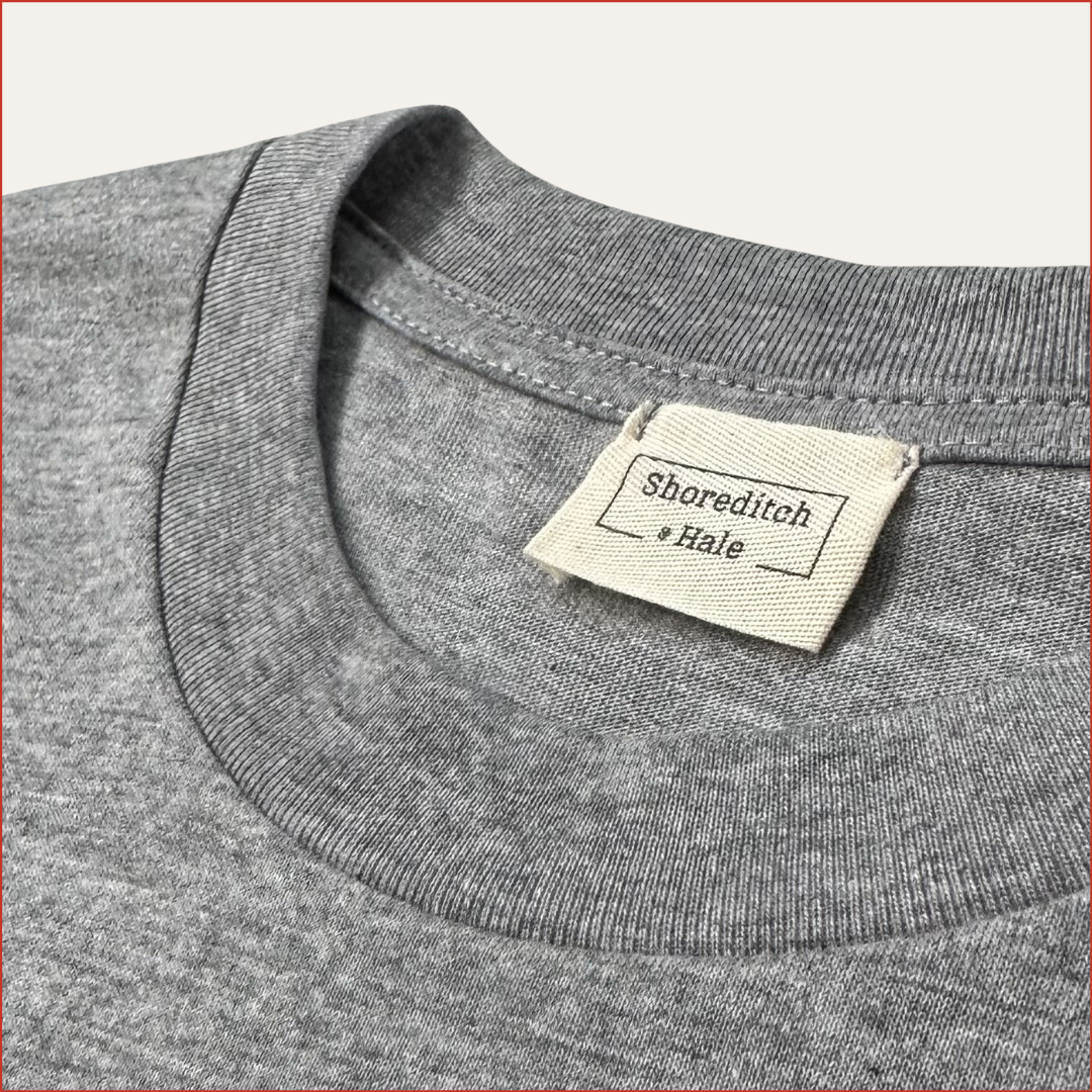 close up of a soft cotton Gray t-shirt with a twill shoreditch and hale label on the collar against a white background. minimalist and understated design by shoreditch and hale
