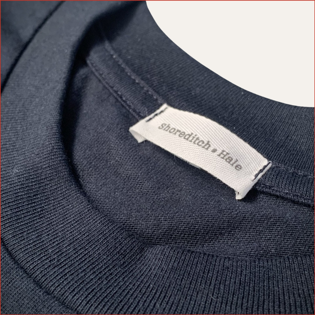 Close-up of a navy tshirt with a 'Shoreditch & Hale' twill label. Minimalist and understated design by shoreditch and hale
