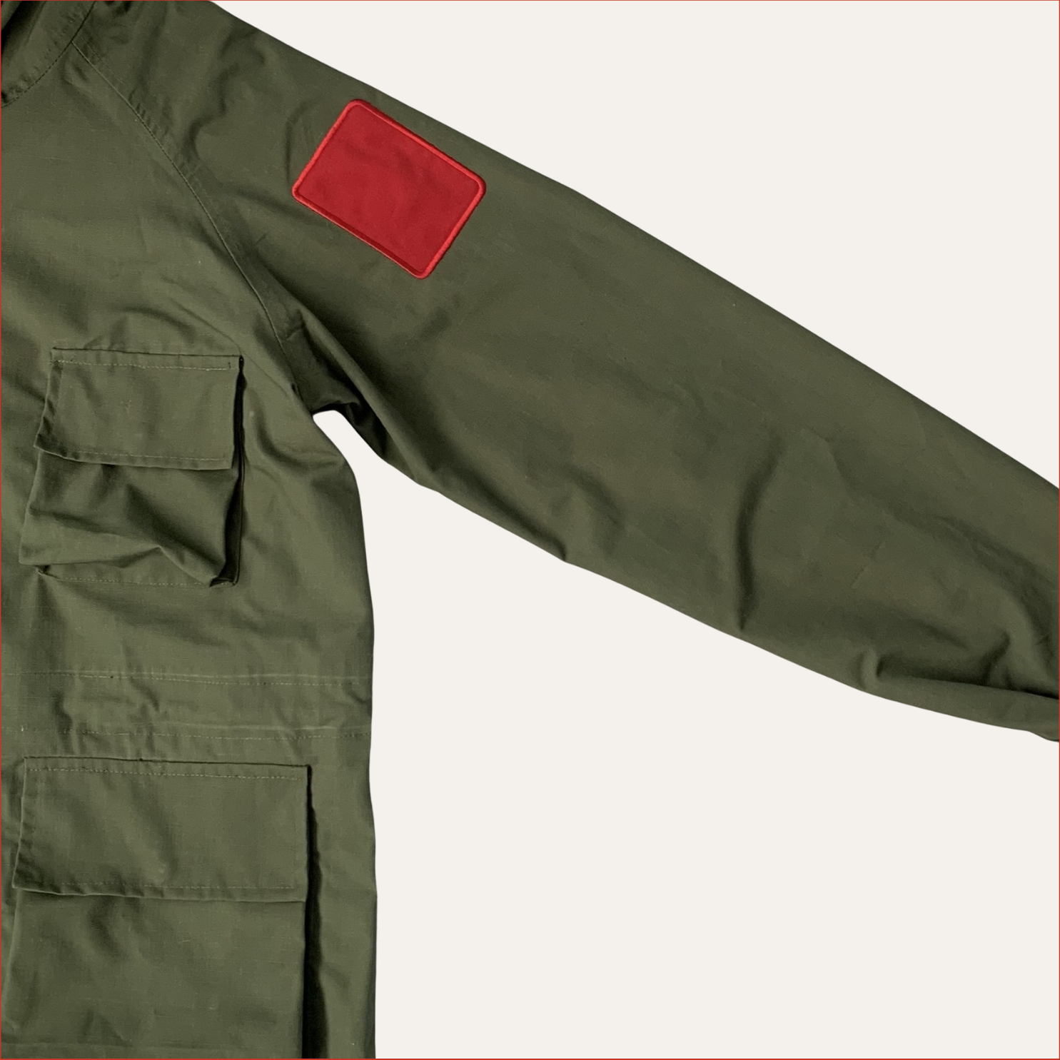 Flat lay photo of a Green Parka jacket by Shoreditch and Hale with red sleeve patches on a white background
