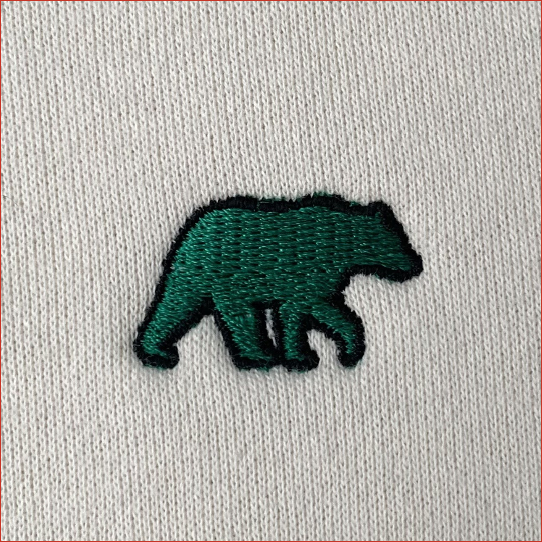 Embroidered green bear design on a light gray fabric background