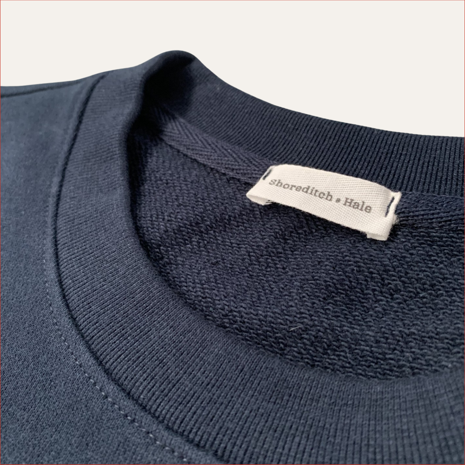 Navy blue sweater with a twill label on the collar against a white background