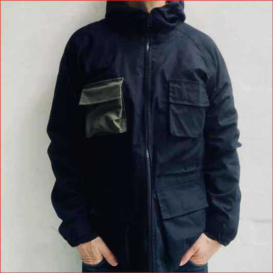 Model wearing a dark blue jacket with a green pocket on a plain background by shoreditch and hale minimalist design