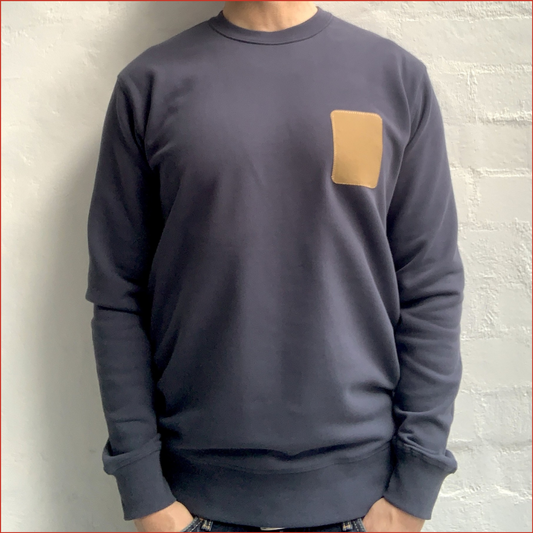 Model wearing a Carbon Blue men's sweatshirt with a brown rectangular patch on a white background. Minimalist design casual wear by shoreditch and hale