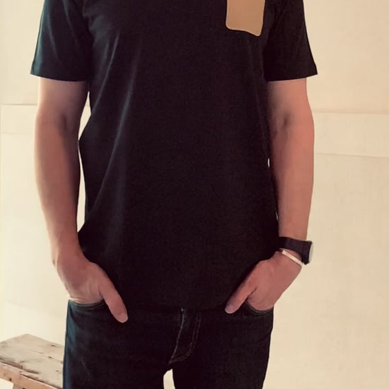 Full length video of a model wearing a a navy Shoreditch and Hale navy t-shirt with a tan embroidered patch on the left chest against a beige background