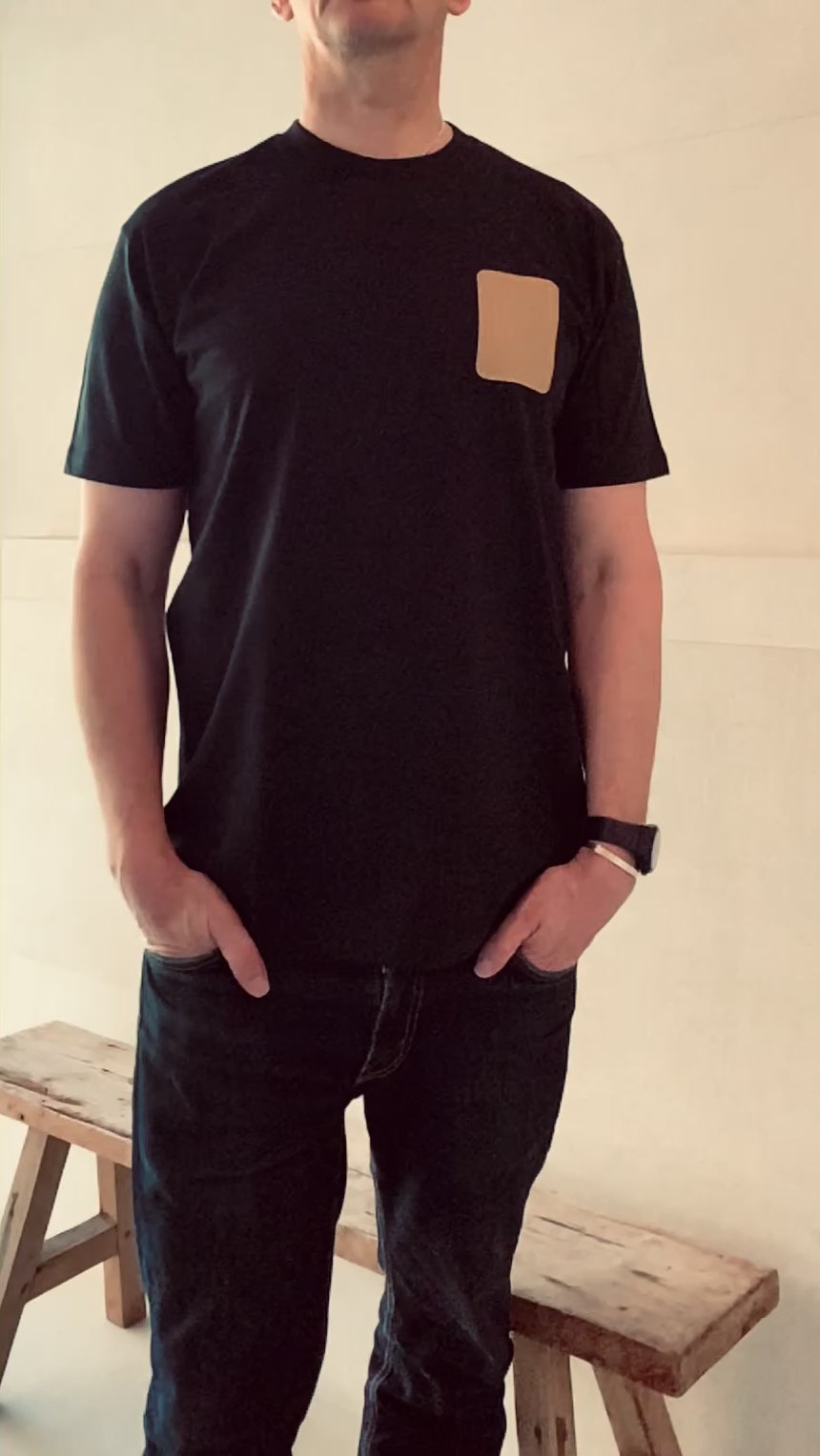 Full length video of a model wearing a a navy Shoreditch and Hale navy t-shirt with a tan embroidered patch on the left chest against a beige background
