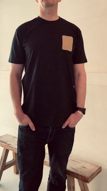 Full length video of a model wearing a a navy Shoreditch and Hale navy t-shirt with a tan embroidered patch on the left chest against a beige background