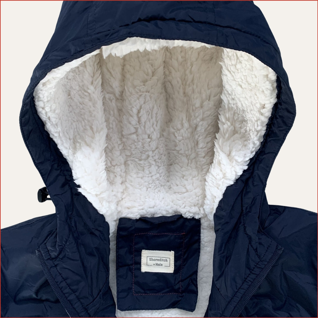 Navy blue Shoreditch and Hale parka with a white fleece inner hood on a white background. Twill label. Minimalist casual design by  Shoreditch and Hale.