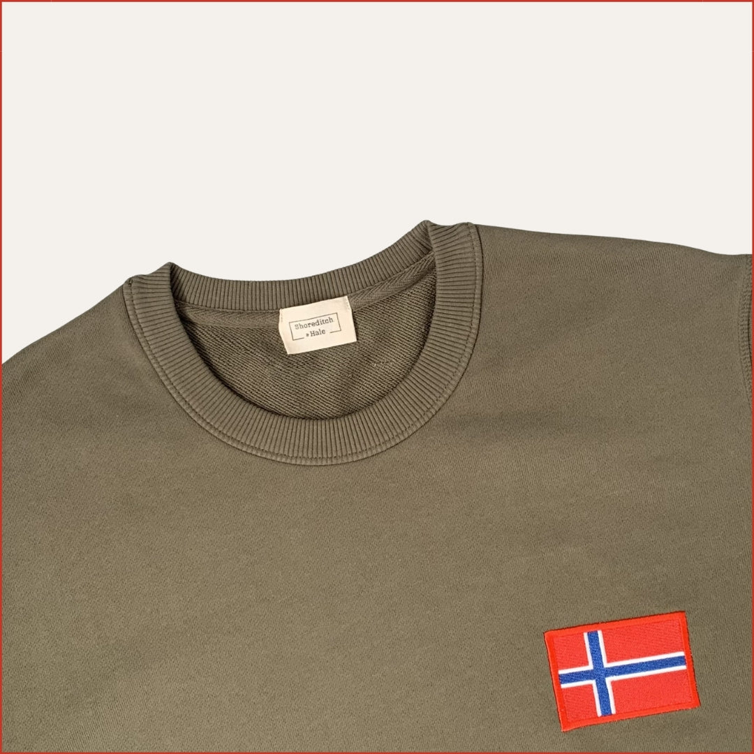 Close up Flay lay image of a shoreditch and hale Green sweatshirt with a small flag patch on a white background. casual menswear