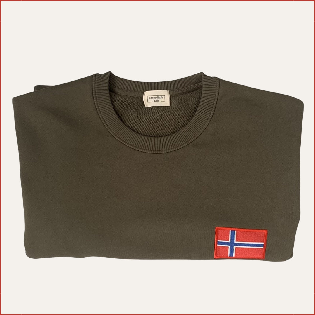 Flay lay image of a folded shoreditch and hale Green sweatshirt with a small flag patch on a white background. casual menswear