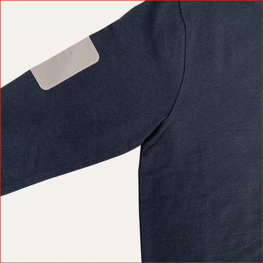 Close up image of a men's Navy blue sweatshirt with a grey colored arm patch on a light gray background. Designed by Shoreditch and Hale