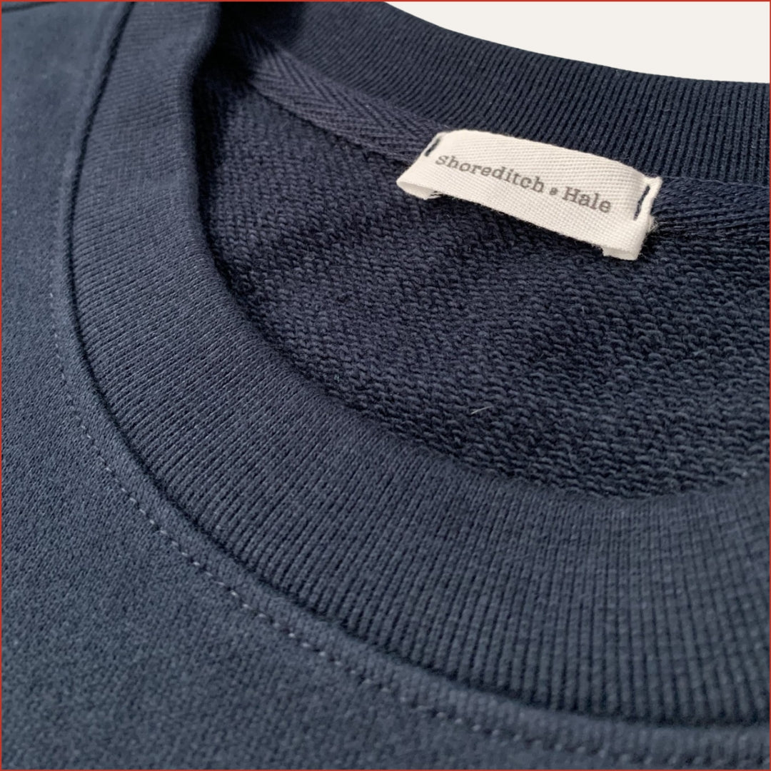 Close-up of a navy blue garment with a shoreditch and hale twill label on the collar.