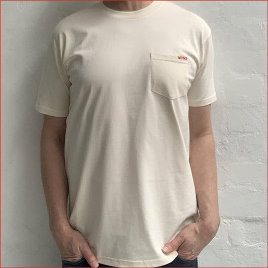 Person wearing a soft white ecru pocket t-shirt with detailed red contrast stitching on the chest against a white background. Minimalist and understated design by shoreditch and hale