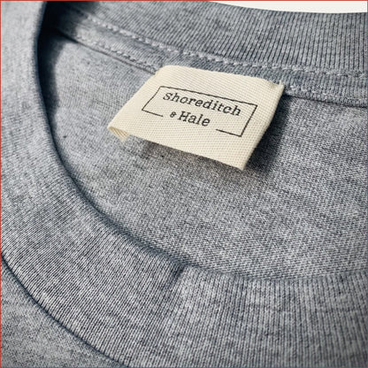 Close-up of a gray tshirt with a 'Shoreditch & Hale' twill label. minimalist and understated design by shoreditch and hale