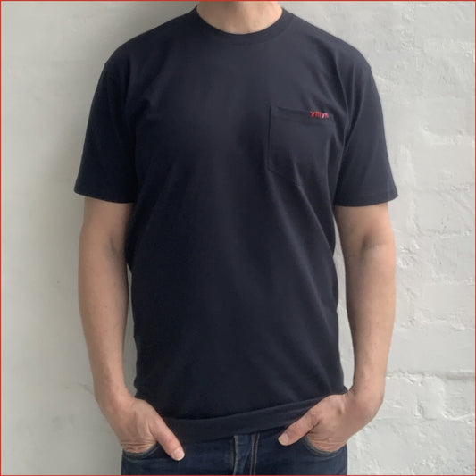 Model wearing a men's soft cotton navy pocket tshirt with contrast red stitching on the chest against a white background. Minimalist and understated design by shoreditch and hale.