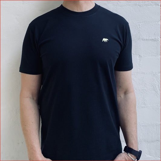 Person wearing a navy t-shirt with a small pastel yellow bear logo on a white background. Minimalist and understated design by shoreditch and hale