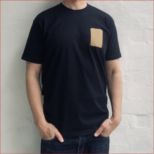 Model wearing a navy t-shirt with a beige patch against a light gray wall. Minimalist and understated design by shoreditch and hale