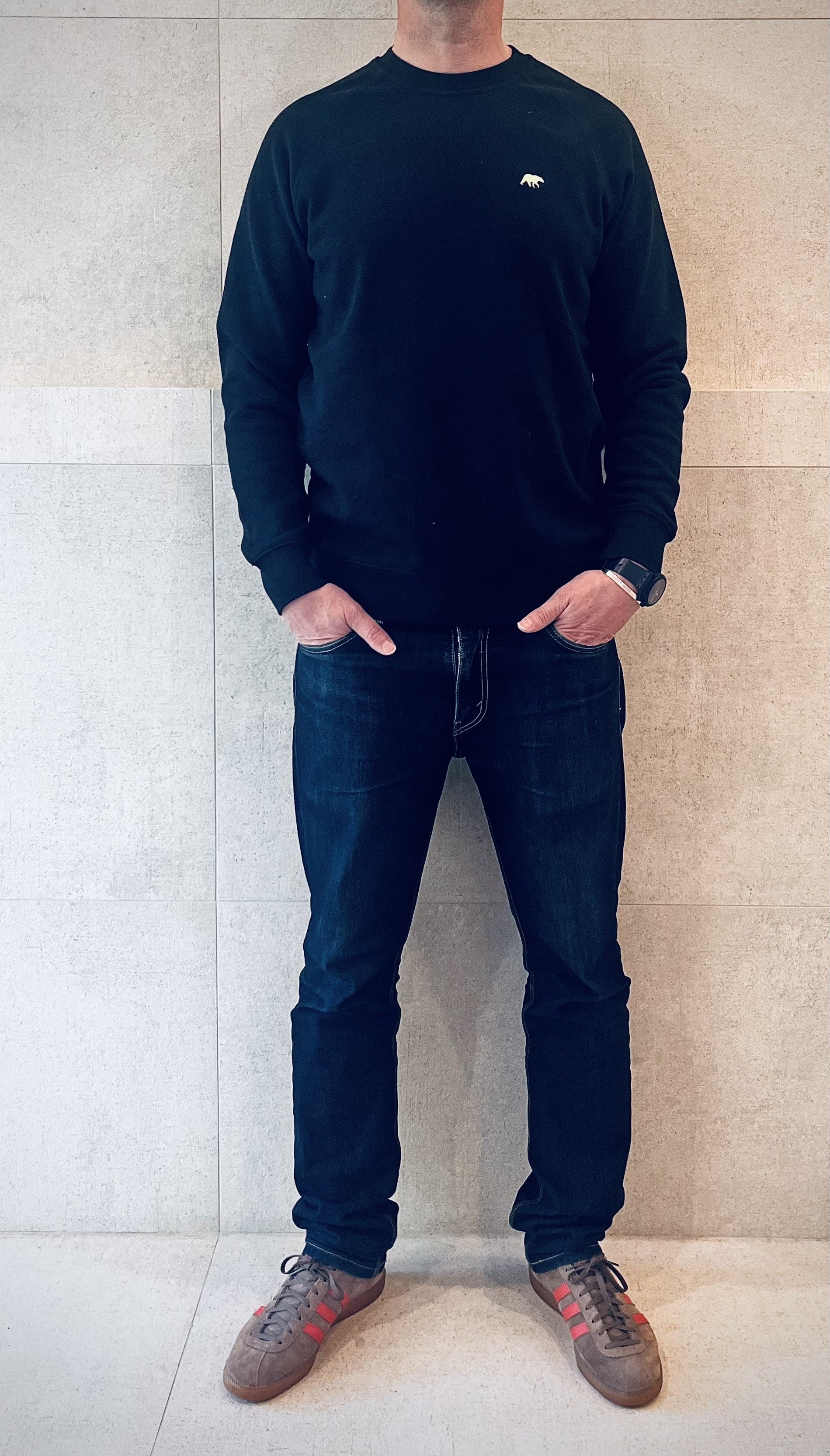 full length Video of Person wearing a Shoreditch and Hale navy long-sleeve sweater and dark jeans standing against a light-colored wall.